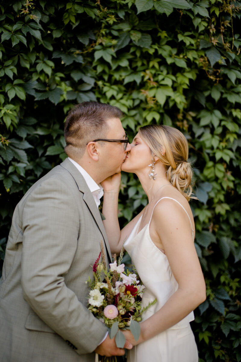 Küssendes Brautpaar bei ihrer standesamtlichen Hochzeit mit einem Brautstrauß