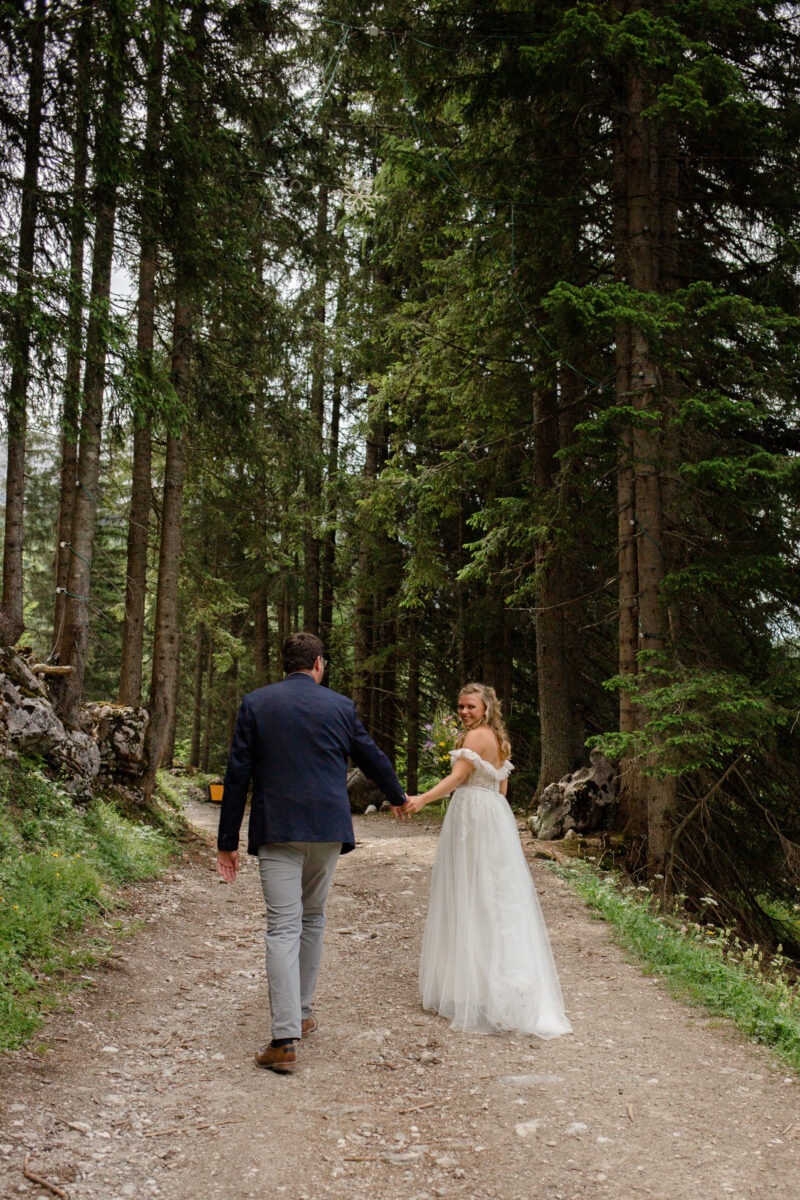 Brautpaar bei ihrer Hochzeit in einem Wald, die Braut blickt verschmitzt in die Kamera, der Bräutigam blickt zu ihr.